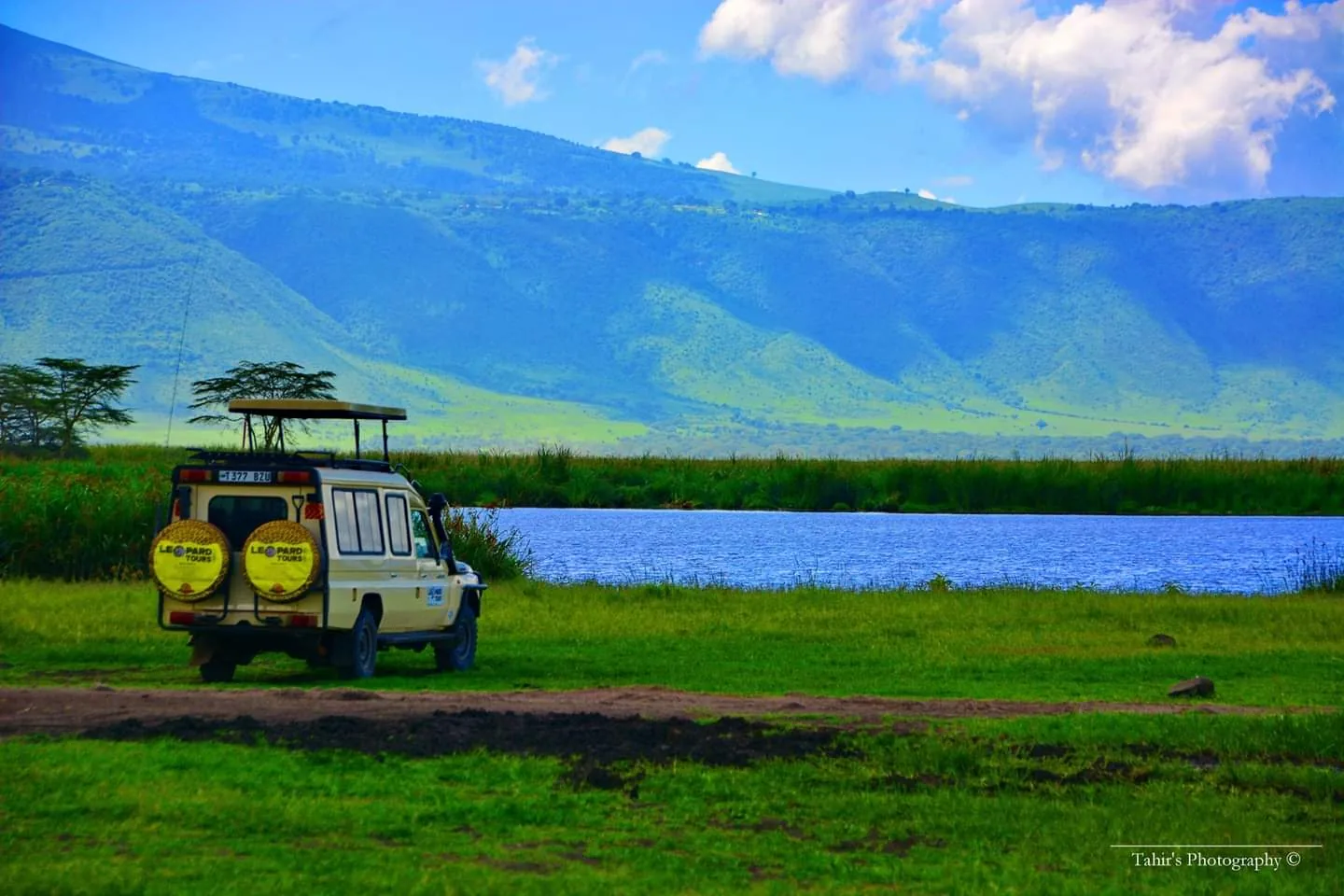 Safari vehicle beside a lake and mountains